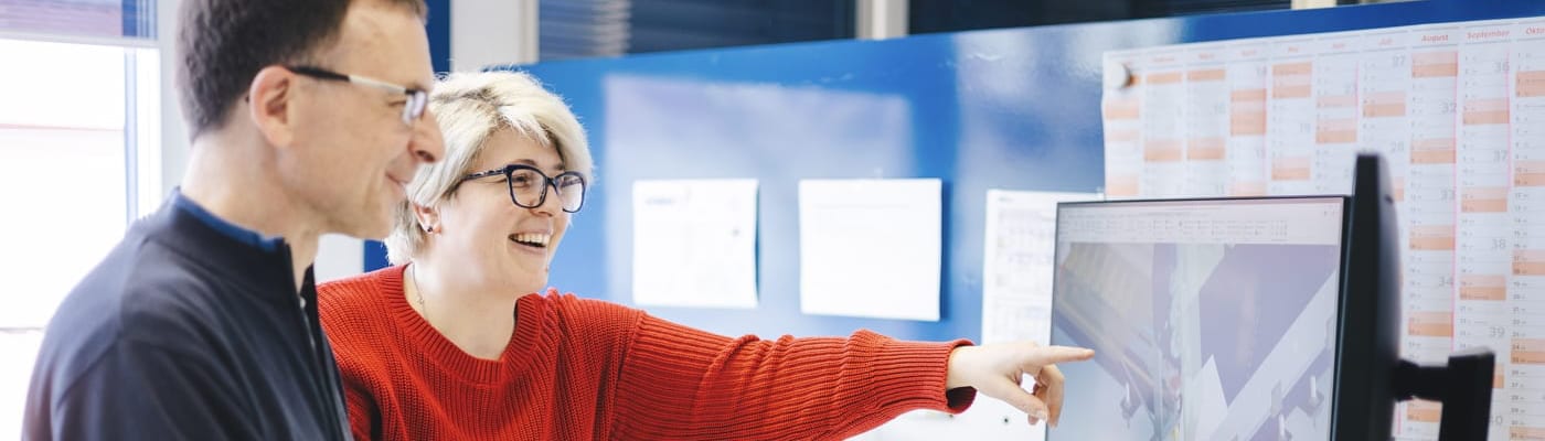 Eine Frau zeigt auf einen Monitor und erklärt einem Mann etwas