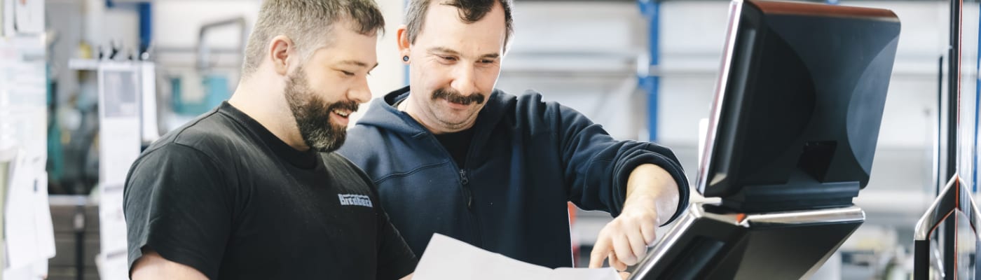 Two men are discussing something in front of a monitor